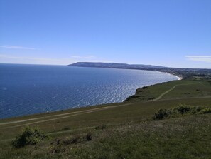 A coastal landscape with a clear view of the sea, a grassy path, and distant hills.