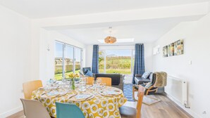 A dining area with a table set for six, large windows, a sofa, and a radiator. - Sea Breeze Your Coastal Sanctuary in Sandown (Sandown)