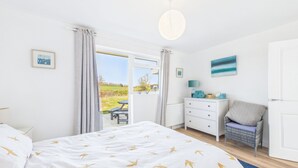 A bedroom with a bed, a dresser, a chair, and a view of the outdoors. - Sea Breeze Your Coastal Sanctuary in Sandown (Sandown)