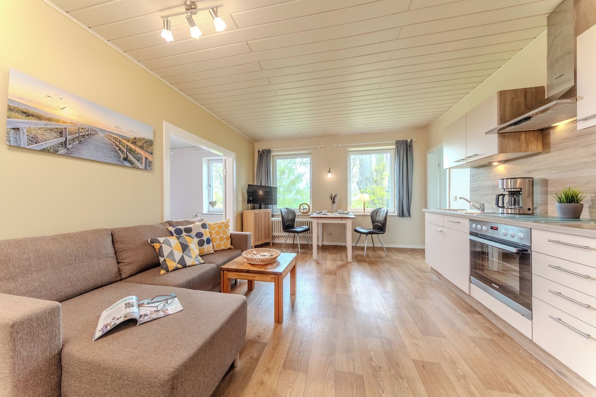 A modern living room with a sofa, coffee table, and a dining area with chairs and a table.