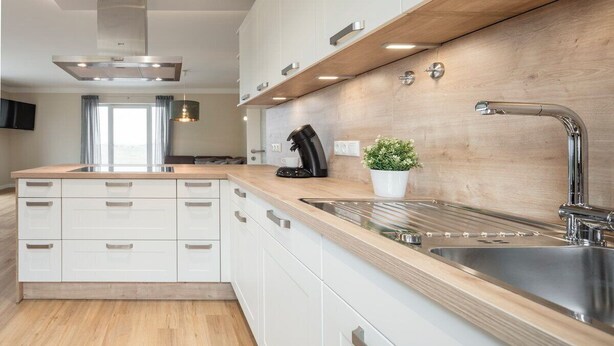 Eine moderne Küche mit weißen Schränken, einer Holzausziehtheke, Edelstahlgeräten und einer eingebauten Spüle.