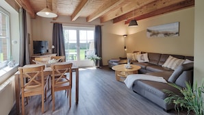 Ein geräumiges Wohnzimmer mit Holzbalkendecke, einer Sofagarnitur, einem Esstisch mit Stühlen und einem Fernseher.