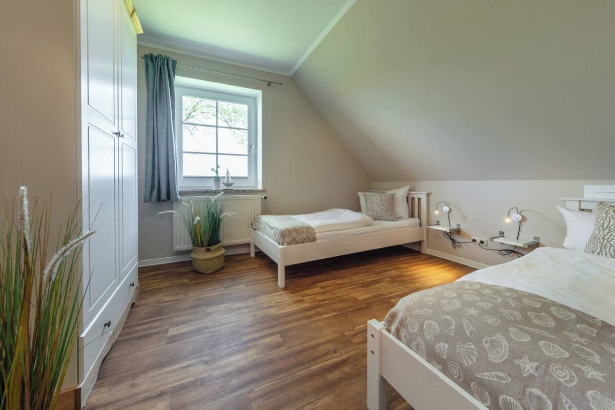 A bedroom with a loft bed, a bedside table with a lamp, a window with curtains, and a radiator.
