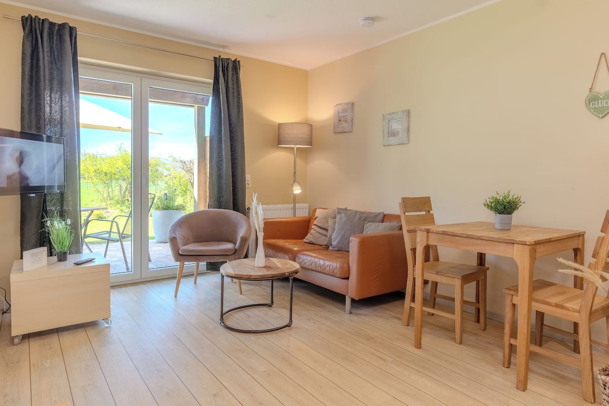 A cozy living room with a sofa, a coffee table, a TV, and a dining area with chairs and a table.