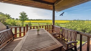 Eine Holzterrasse mit Tisch und Bänken, mit Blick auf ein grünes Feld und einen klaren Himmel.