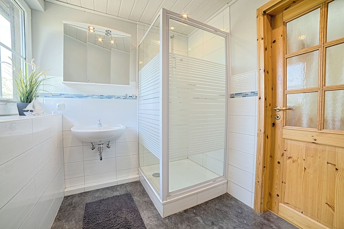 A bathroom with a white sink, a glass shower enclosure, and a wooden door.