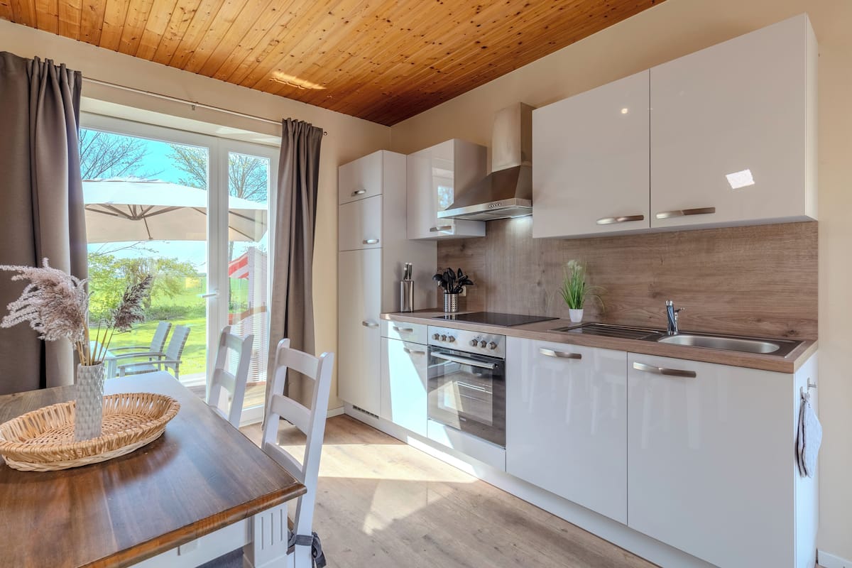 A modern kitchen with white cabinets, a built-in oven, and a large window.