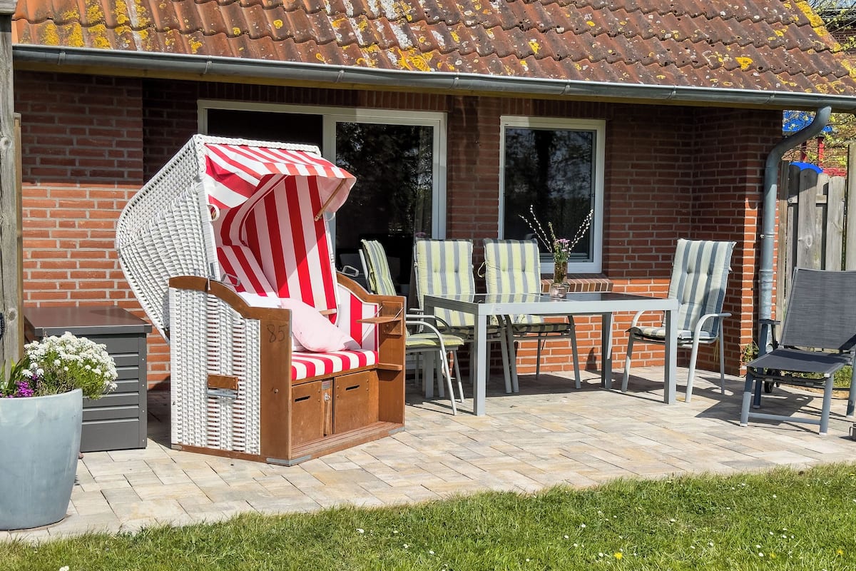A patio with wicker chairs and a table, a brick house, and a grassy area.