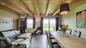 Ein modernes Wohnzimmer mit Holzboden, einem schwarzen Ledersofa, einem Holzesstisch und einem großen Fenster mit Blick.