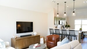 Un salon moderne doté d’un téléviseur à écran plat, d’un fauteuil en cuir, d’un canapé et d’un coin repas avec des chaises et une table.