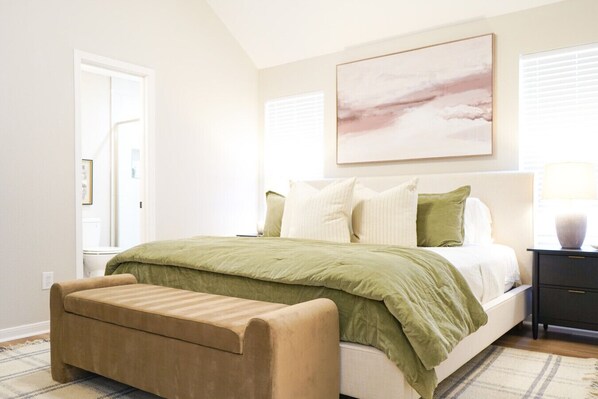 Un dormitorio con cama, un banco, una mesita de noche, una lámpara y un cuadro en la pared.