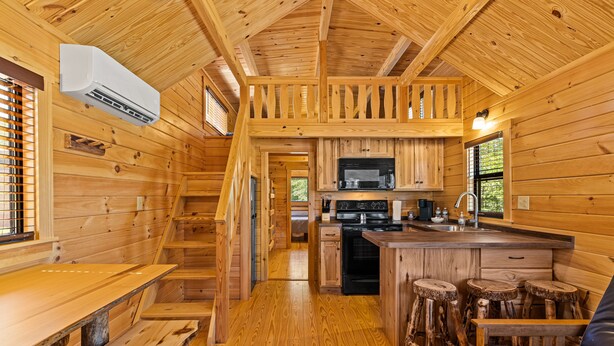 Interior de una cabaña de madera con cocina, comedor y escalera.