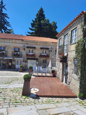 Un patio con suelo de piedra, mobiliario exterior y un edificio con varias tiendas y cafeterías.