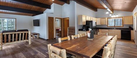 A spacious dining area with a large wooden table and benches, a kitchen with wooden cabinets, and a ceiling with exposed beams.