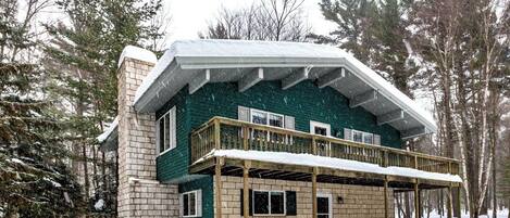 A two-story house with a balcony, surrounded by snow and trees.
