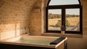 A bathroom with a bathtub, a window with a view of a field, and a potted plant. - Masseria Surace (Noci)