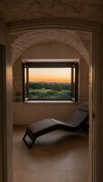 A room with a view of a sunset over a landscape, a reclining chair, and a small potted plant.