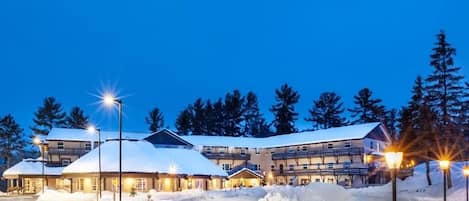 A multi-story hotel with a snow-covered roof, surrounded by snow, and illuminated by street lamps.