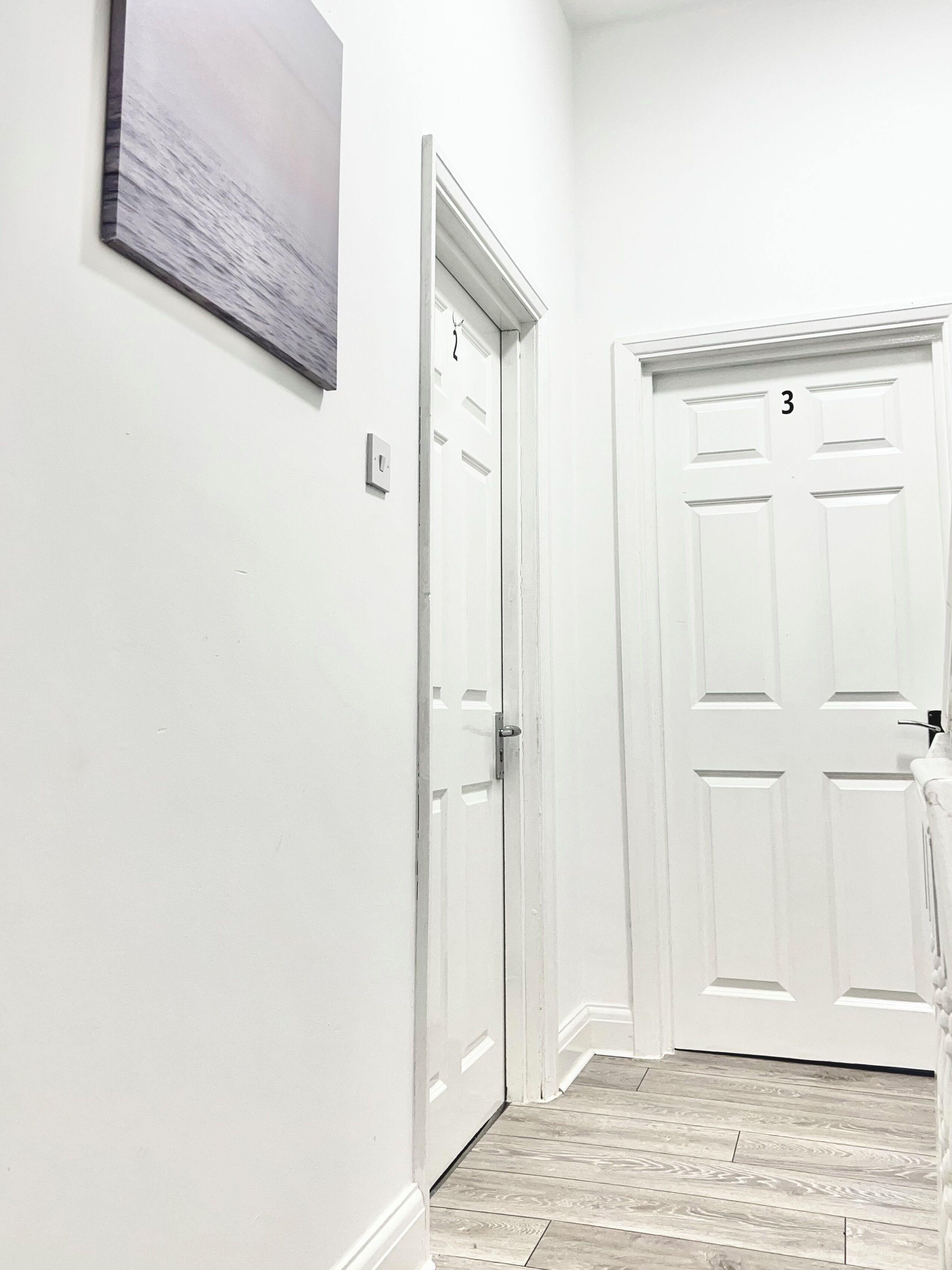 A hallway with white doors, one marked with the number 3, and a light switch on the wall.