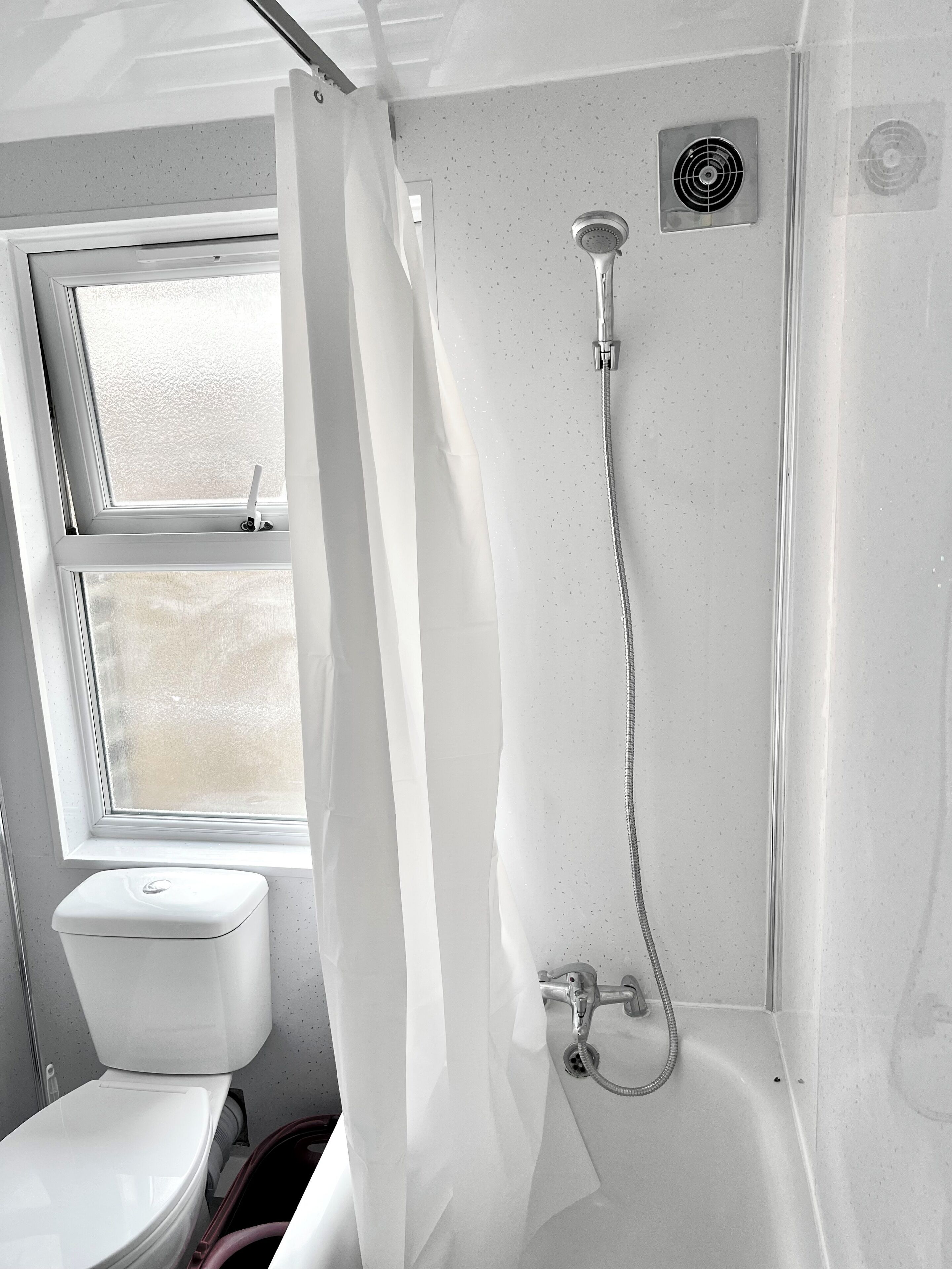 A bathroom with a shower, toilet, and window.