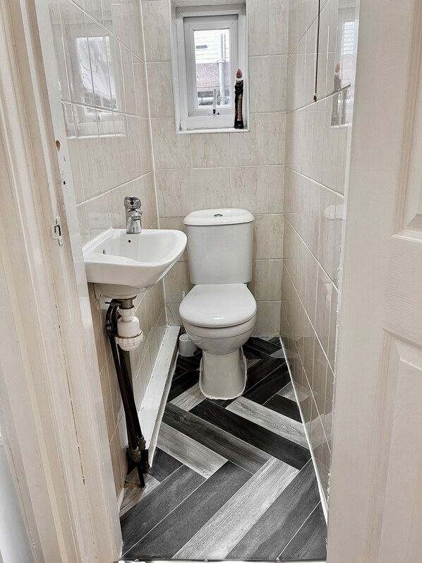 Une petite salle de bain avec un lavabo blanc, des toilettes et une fenêtre située au-dessus des toilettes.