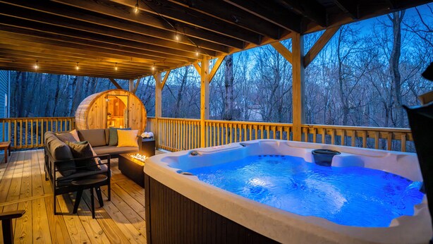 A wooden deck with a hot tub, outdoor seating, and a view of trees.