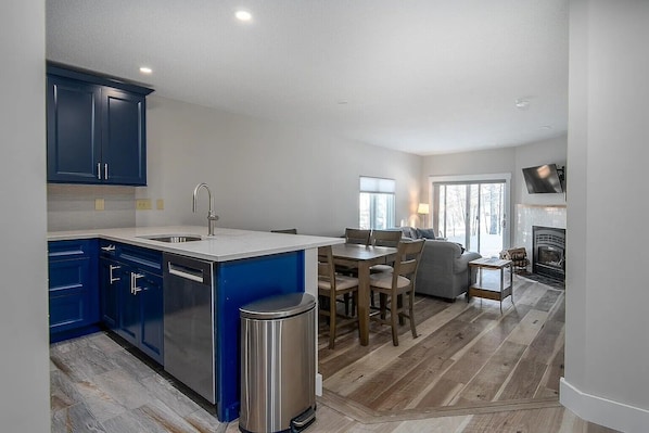 Een moderne keuken met blauwe kastjes, een centraal eiland en een zithoek met een bank en stoelen.