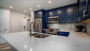 A modern kitchen with dark blue cabinets, stainless steel appliances, and a white marble countertop.