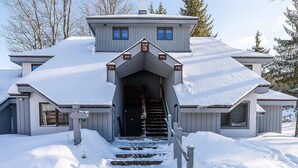 A two-story house with a steeply pitched roof covered in snow, a front entrance with a staircase, and a sign indicating the house is a village center.