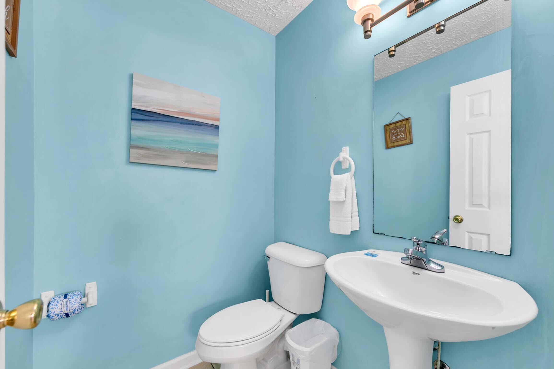 A bathroom with a light blue wall, a white toilet, a white sink, and a mirror above the sink.