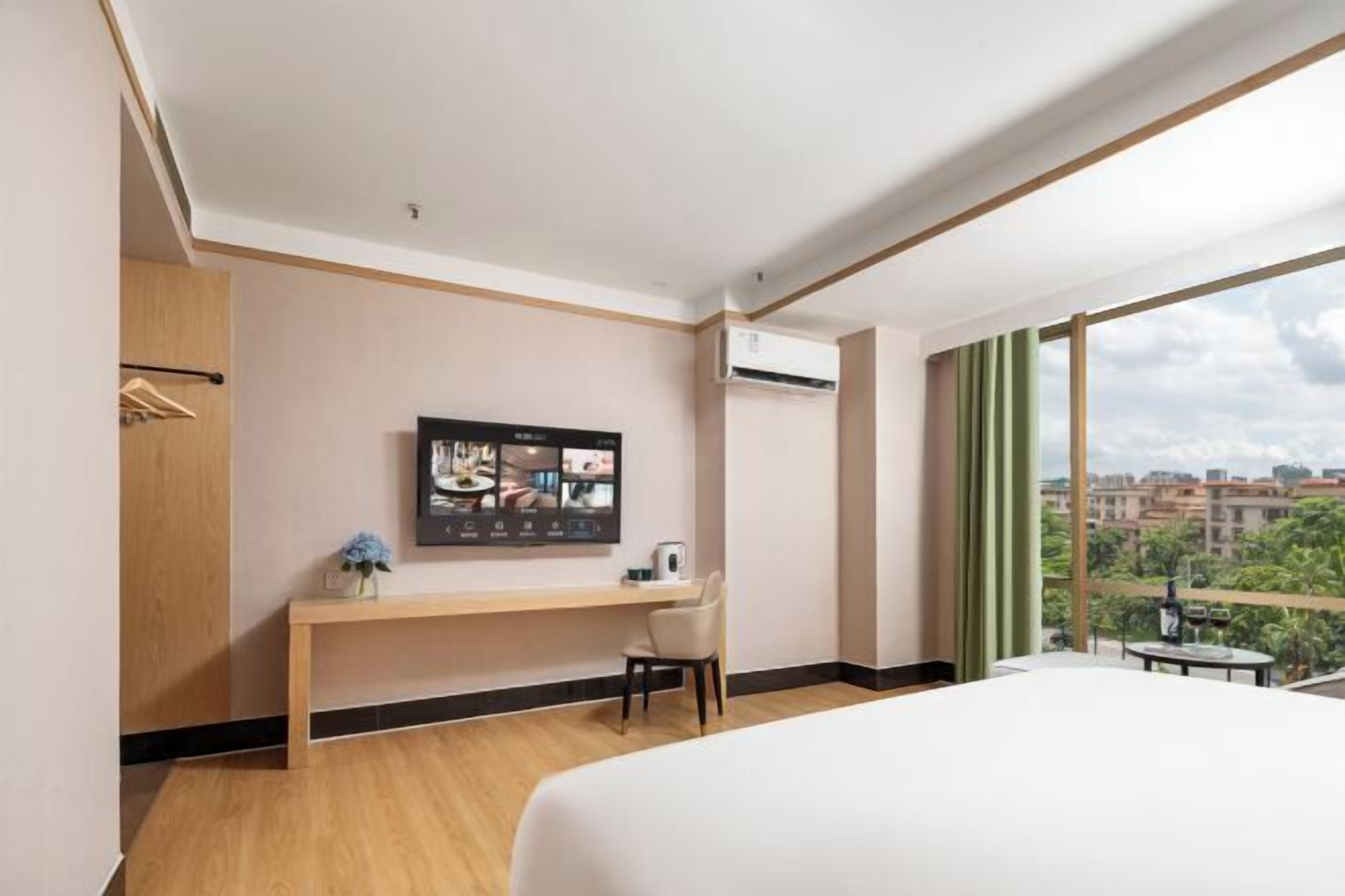 A hotel room with a bed, a desk, a chair, a TV mounted on the wall, and a window with a city view.