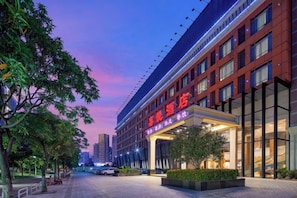 A hotel with a modern facade, a prominent entrance, and a landscaped area with trees. - Joy Hotel (Foshan Nanhai Pengruili Jihua Plaza) (Foshan)