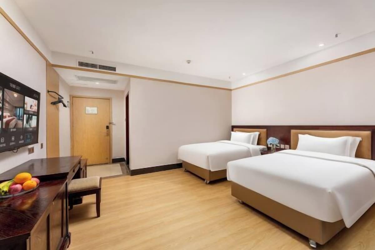 A hotel room with two single beds, a wooden desk with a chair, and a television on the wall.