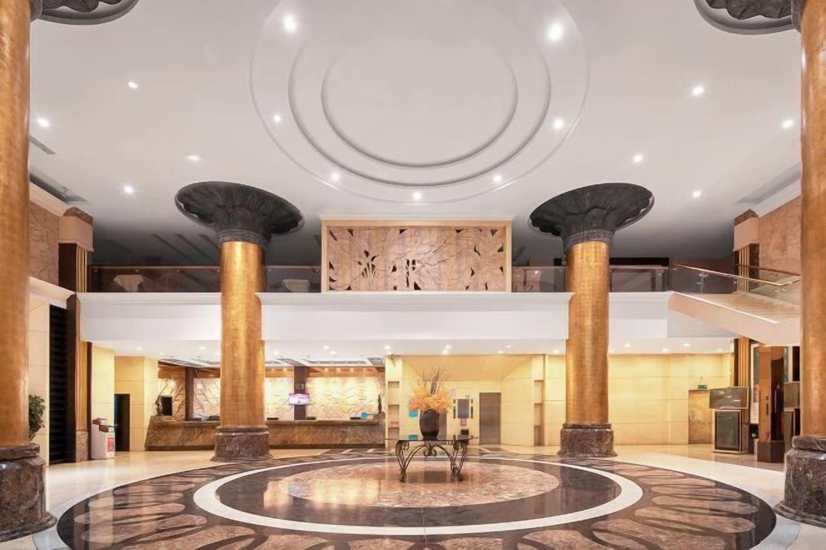 A spacious lobby with a central circular marble floor, large columns, and a reception desk.