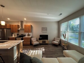 Un salon moderne comprenant un canapé, un téléviseur et un coin cuisine avec des meubles en bois et un réfrigérateur.