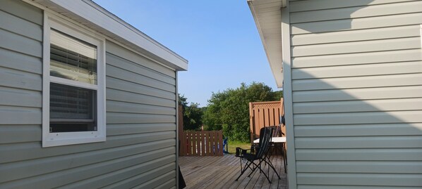 A deck area with a table and chairs, surrounded by a wooden fence and greenery.