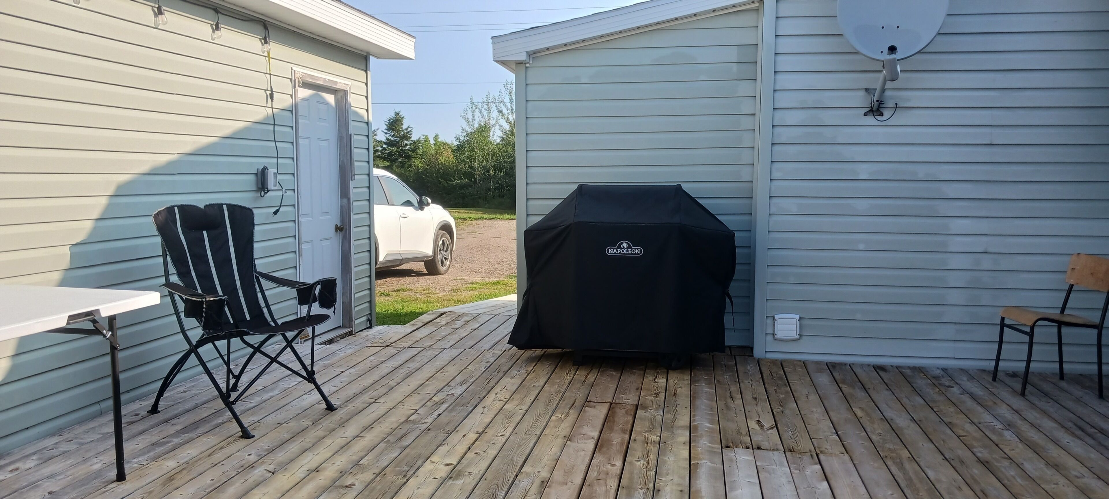 A covered barbecue grill, a folding chair, and a table on a wooden deck.