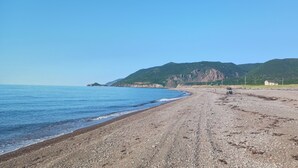 A pebbly beach with a clear view of the sea and distant mountains.