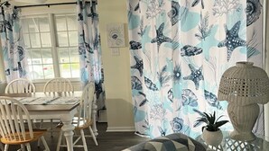 A dining area with a table and chairs, a patterned curtain, and a wicker lamp. - Charming 3-bedroom condo with AC, WiFi in brilliant Wildwood Crest (Wildwood Crest)