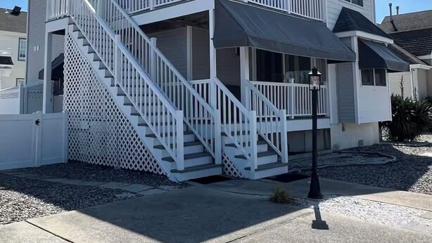 A two-story house with a covered front porch and a staircase leading to the upper level. - Charming 3-bedroom condo with AC, WiFi in brilliant Wildwood Crest (Wildwood Crest)