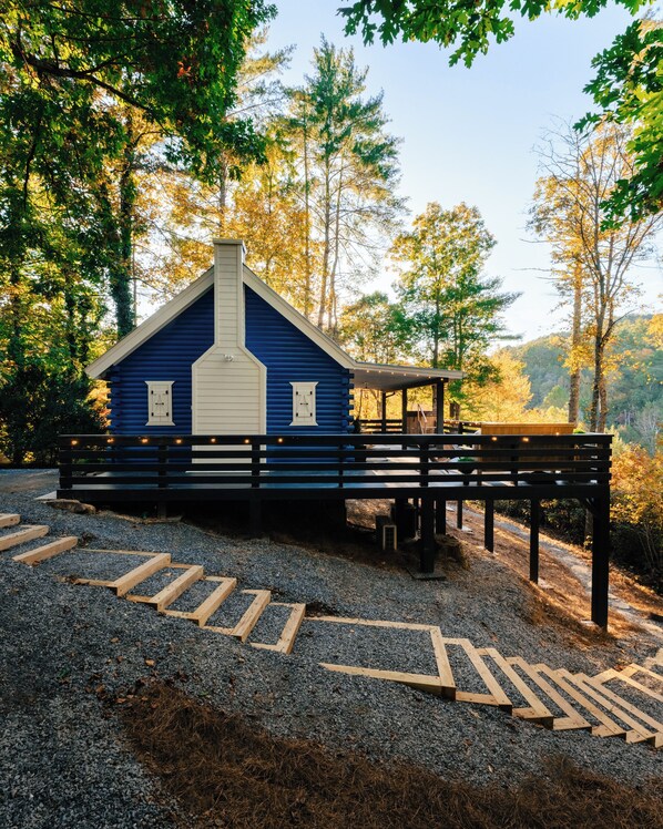 A rustic cabin with a sloped roof and a chimney, surrounded by a gravel path and wooden steps leading to a bench. - Blue’s Nook: Mountain View’s, Cedar Barrel Hot Tub, and close to Downtown (Blue Ridge)