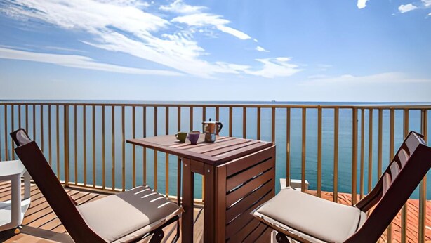 A wooden deck with two lounge chairs and a table, overlooking a body of water.