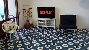 A living room with a patterned floor, a television displaying 'NETFLIX', a chair, and a small table with decorative items.