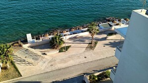 A coastal hotel with a view of the sea, outdoor seating, and a staircase leading to the beach.