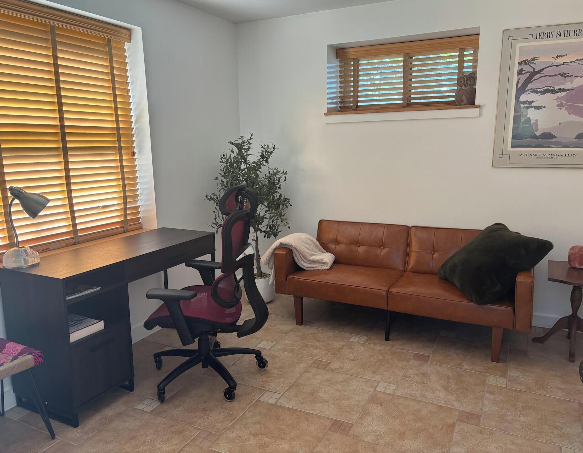 Une pièce comprenant un bureau, un fauteuil de bureau, un canapé en cuir marron et une petite table sur laquelle est posée une plante.