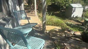 A patio with two blue metal chairs and a small shed in a garden setting.