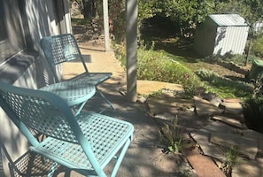 Um pátio com duas cadeiras de metal azuis e um pequeno galinheiro em um jardim.