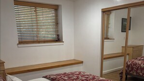 A bedroom with a bed, bedside lamp, and a window with blinds.