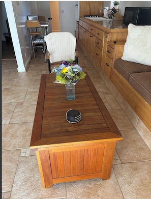 Uma mesa de centro de madeira com um vaso de flores no centro, uma cadeira e um sofá numa sala de estar.
