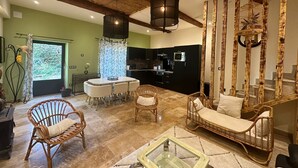 A modern living room with a dining area, wicker furniture, a glass coffee table, and a kitchen in the background. - La villa verte Domaine de la tapie de Bouchet - in the Camargue (Arles)